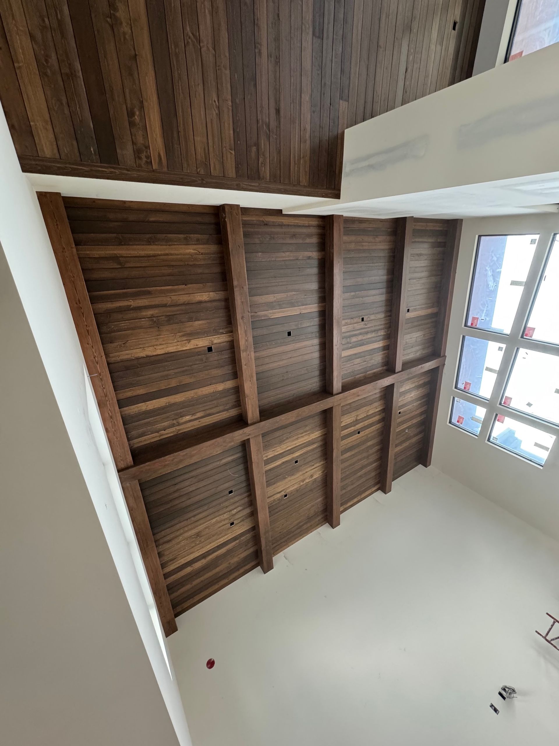 Tilted view of a room ceiling with exposed dark wooden beams and a bright window on the right.
