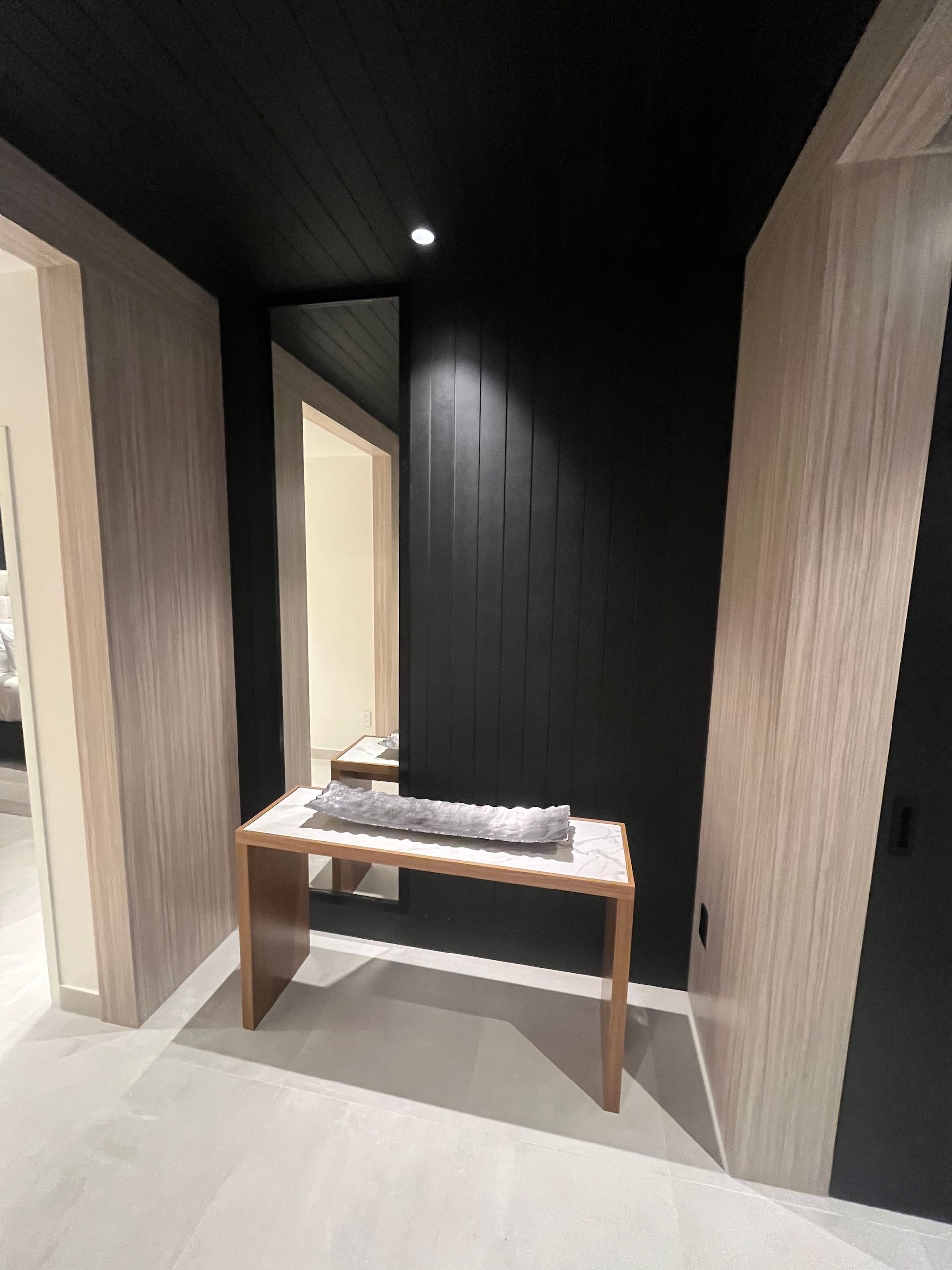 Modern hallway with black walls, light wood doors, and a small console table under a ceiling light.