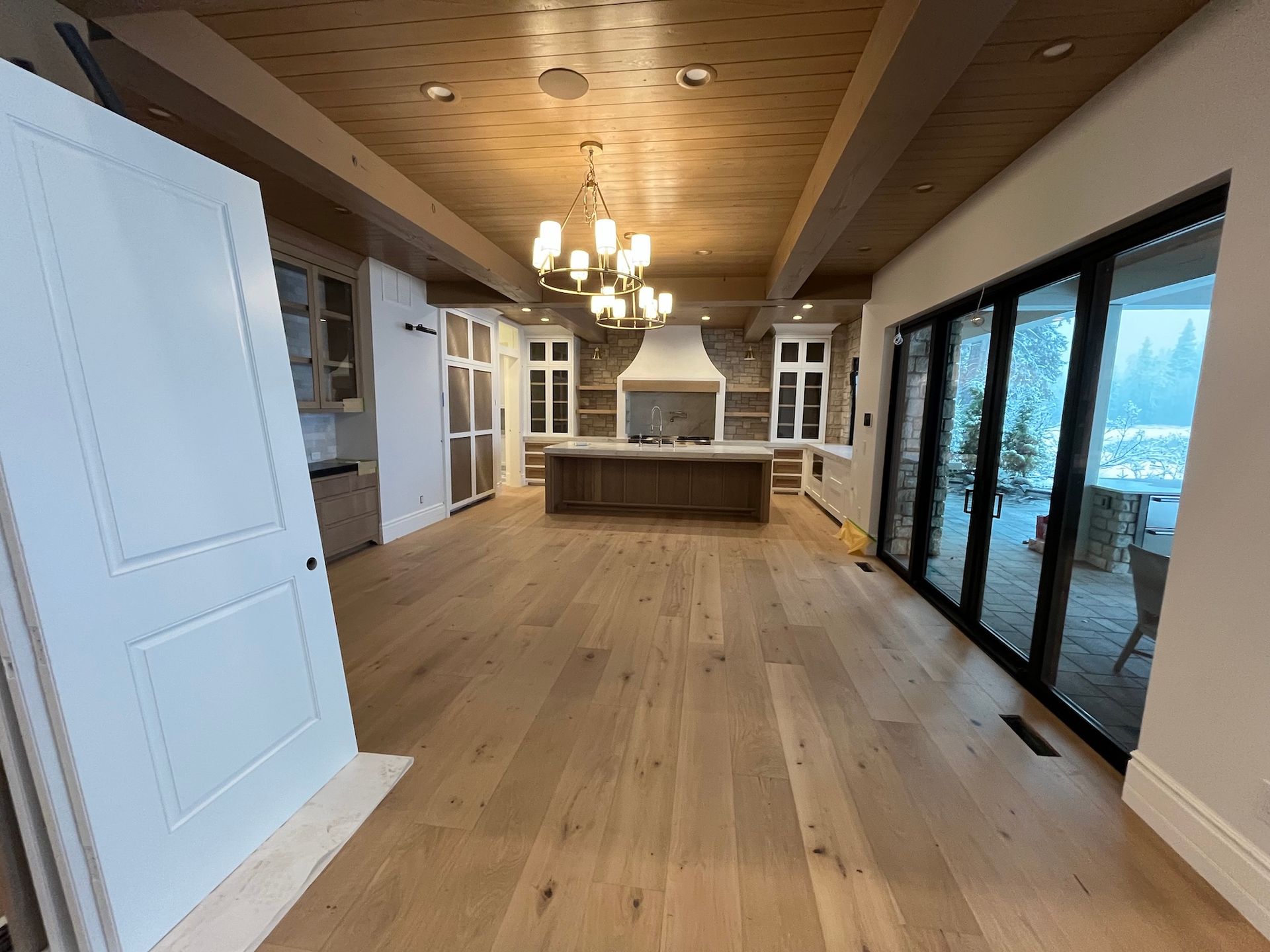 Spacious modern kitchen with wood floors, island, chandeliers, and glass doors to a mountain view