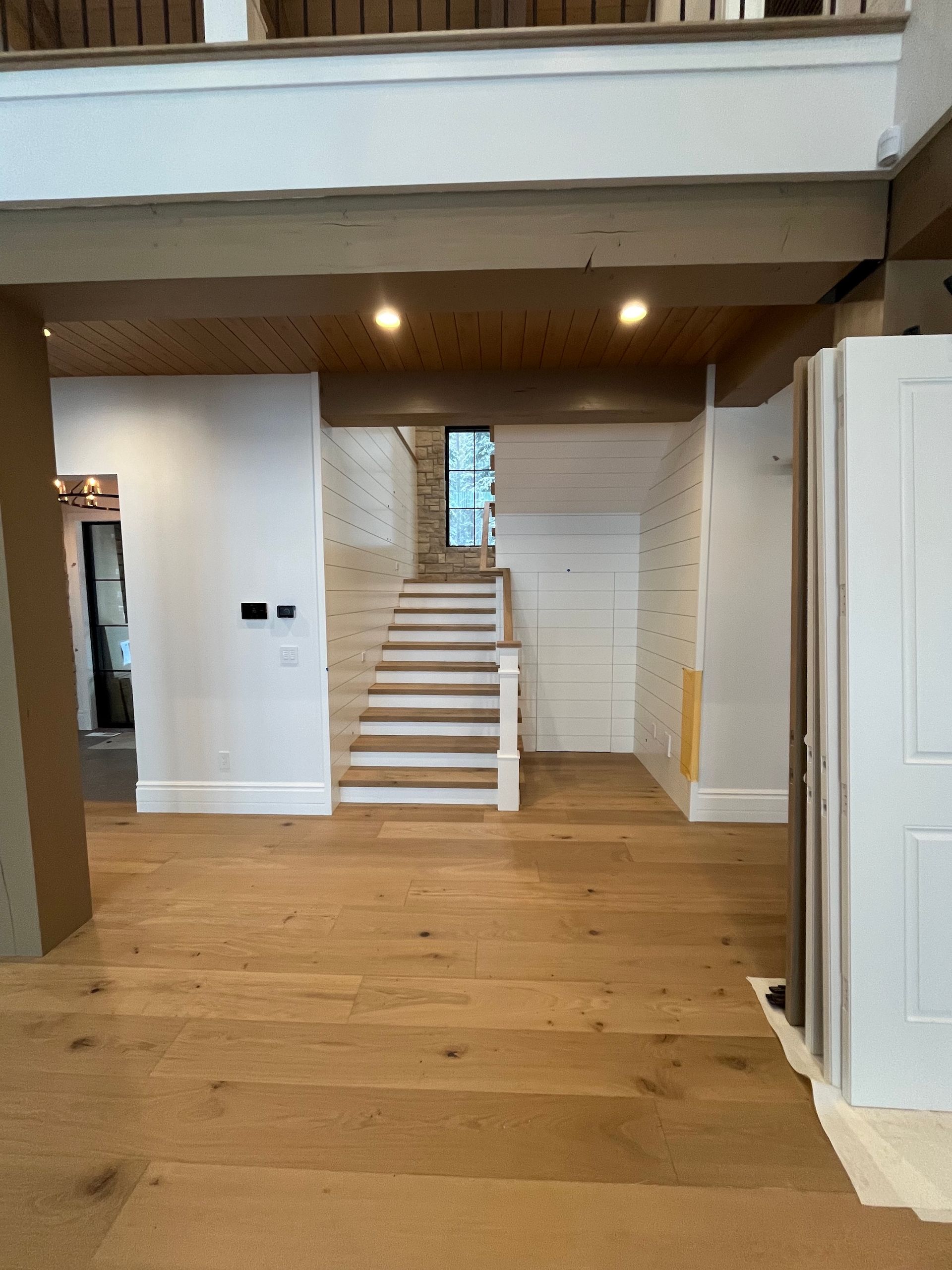 Open-plan interior with hardwood floor, staircase, and white walls under dark exposed beams