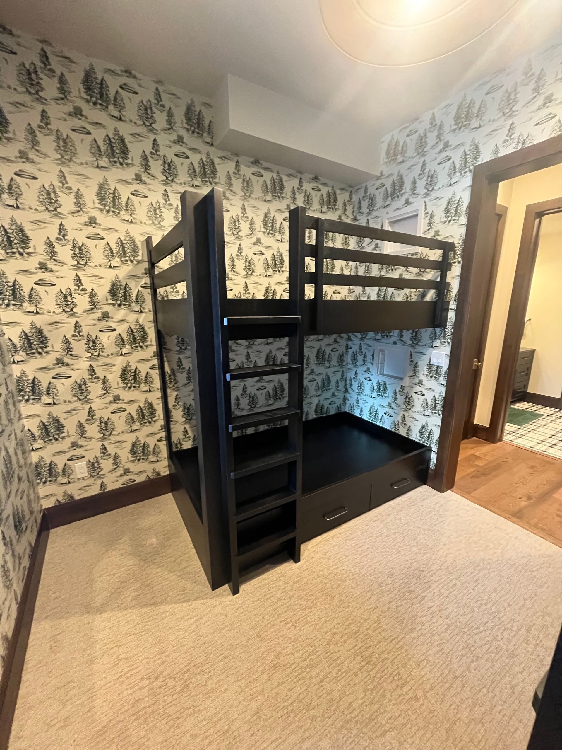 Black wooden bunk bed in a wallpapered room with beige carpet and hardwood floor.