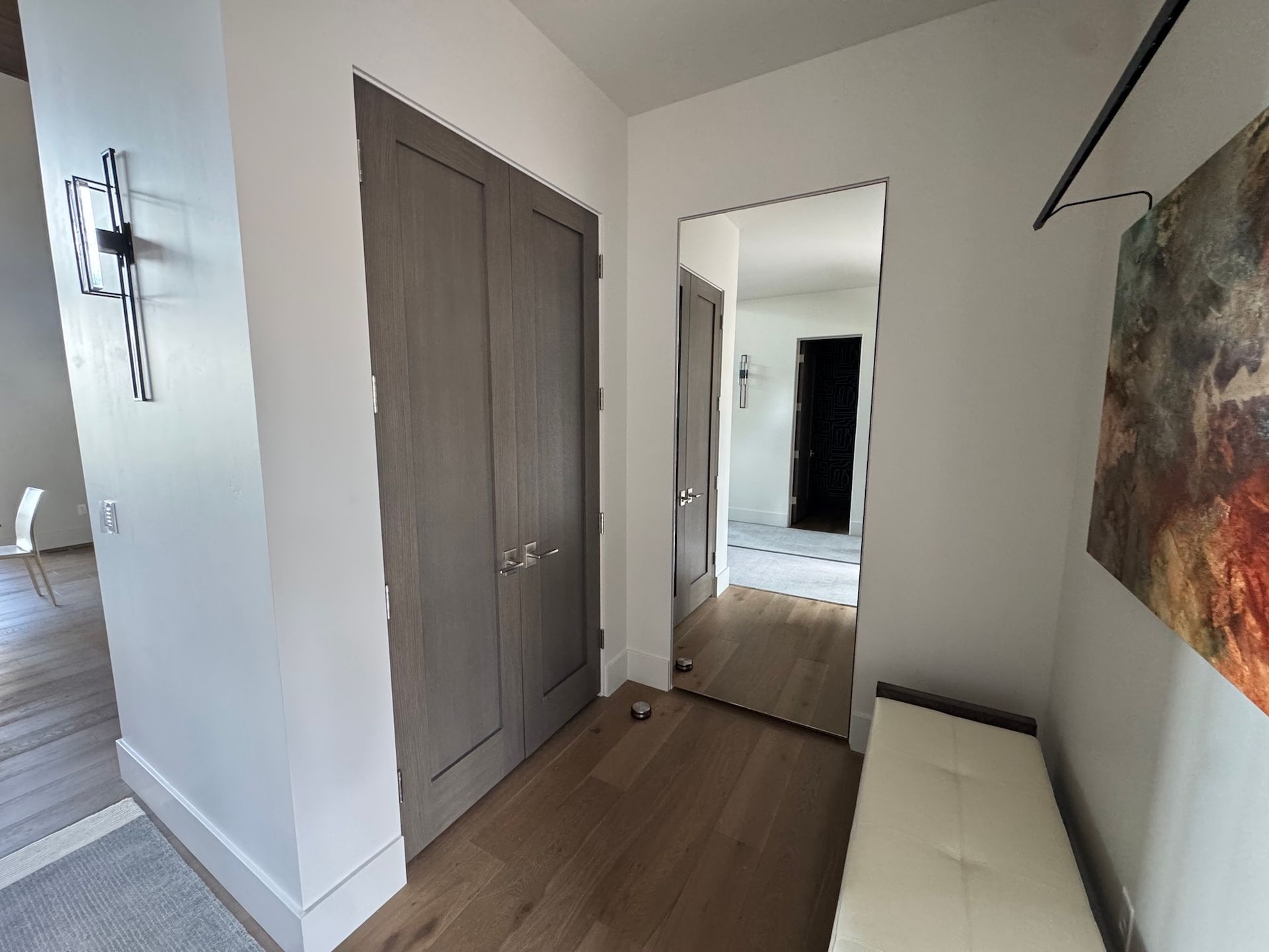 Hallway with gray double doors, mirror, white bench, and abstract wall art.