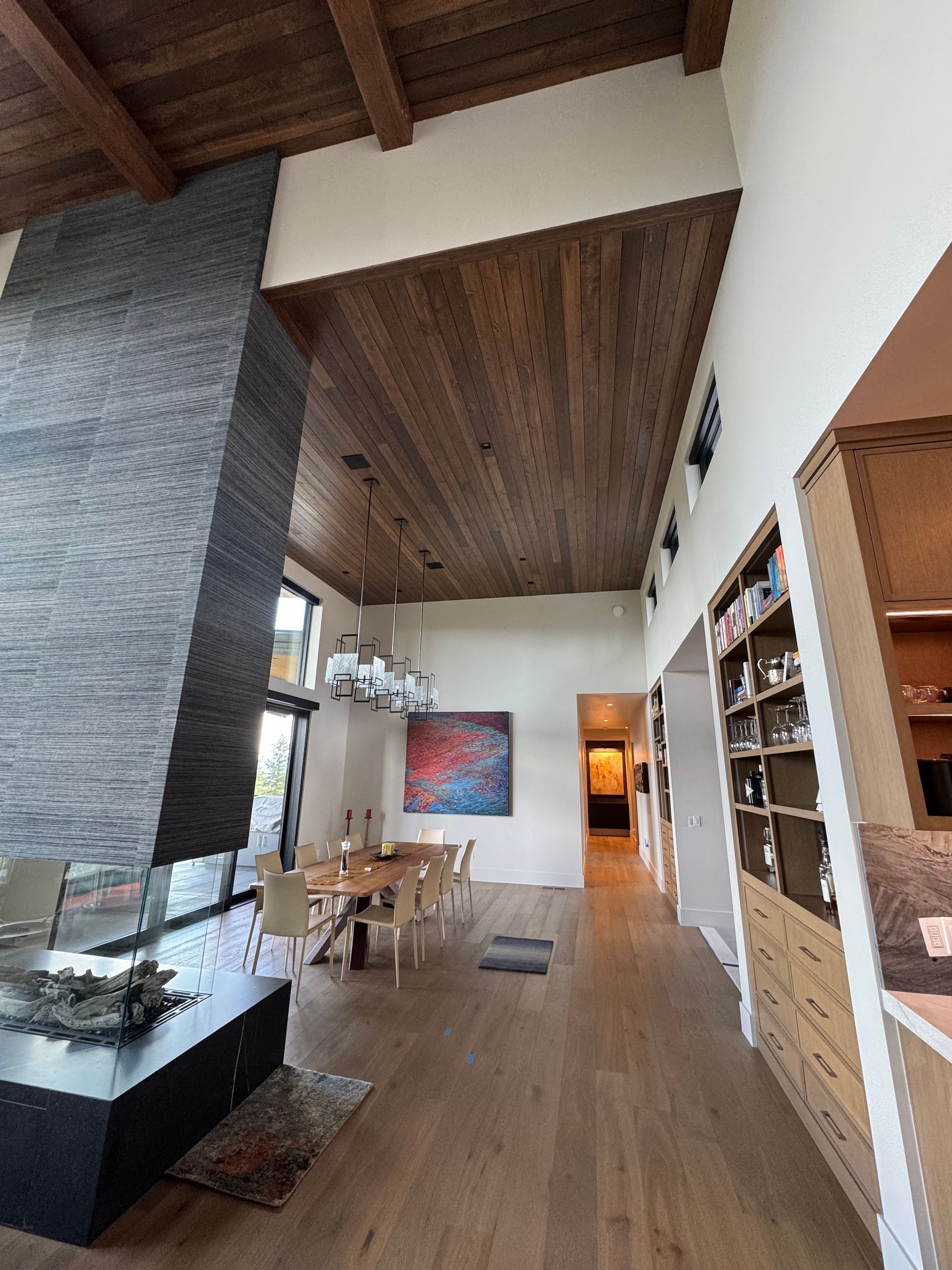 Modern living room with wood ceiling, fireplace, dining table, and built-in shelving