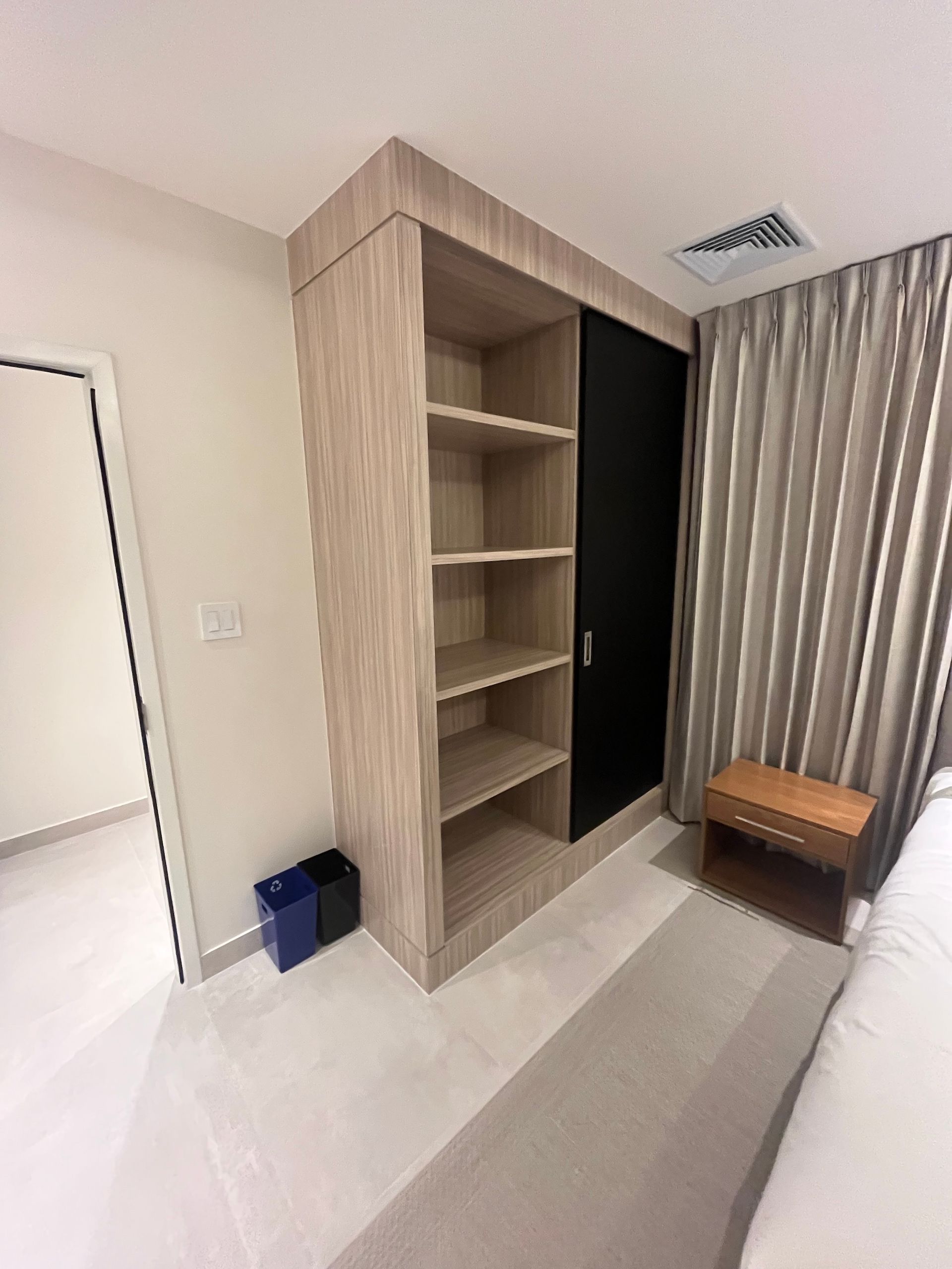 Built-in wood wardrobe with shelves, beside a curtained window and small bench in a bright bedroom.