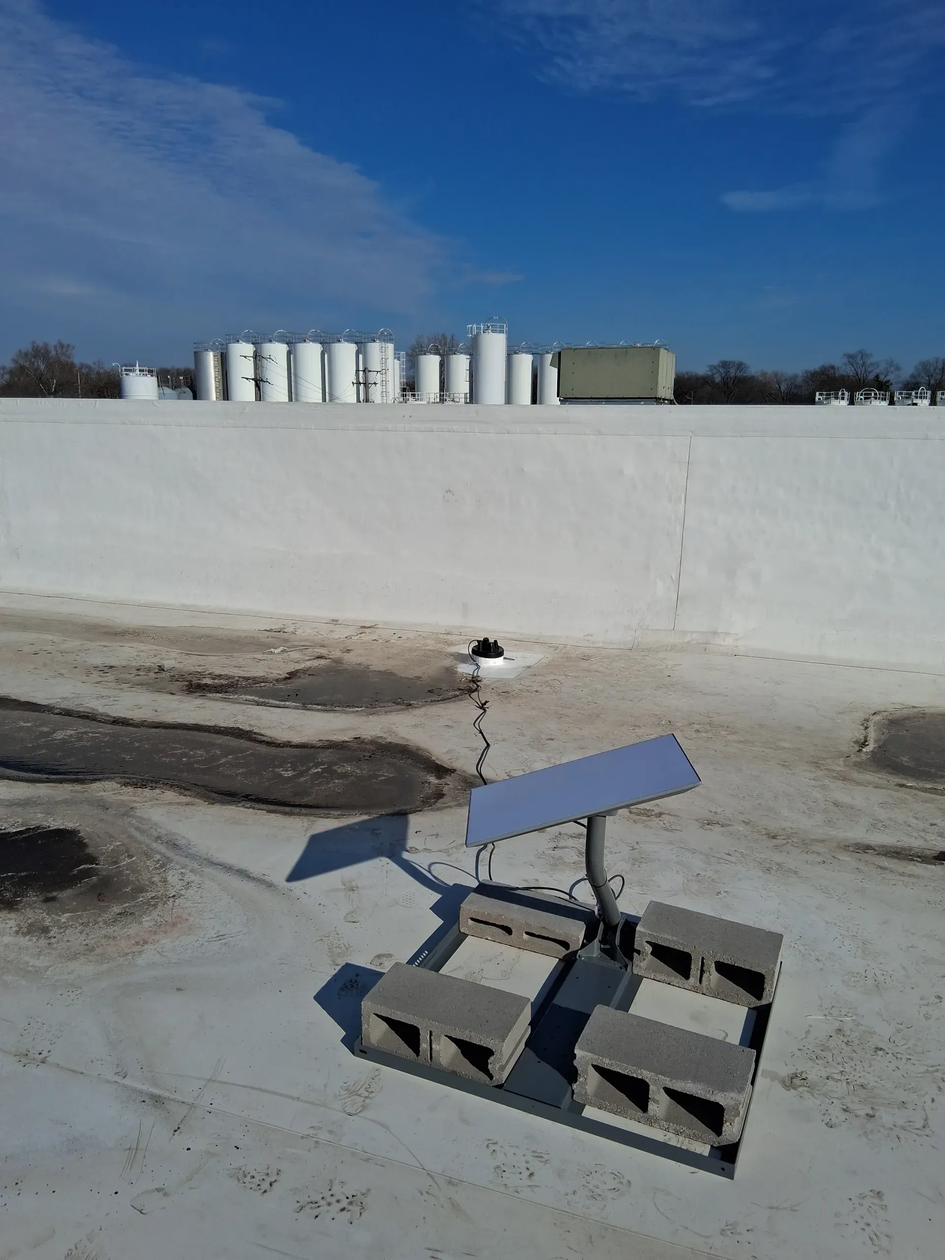 A Starlink satellite dish mounted on a flat roof using a concrete block base, with vent pipes in the background.
