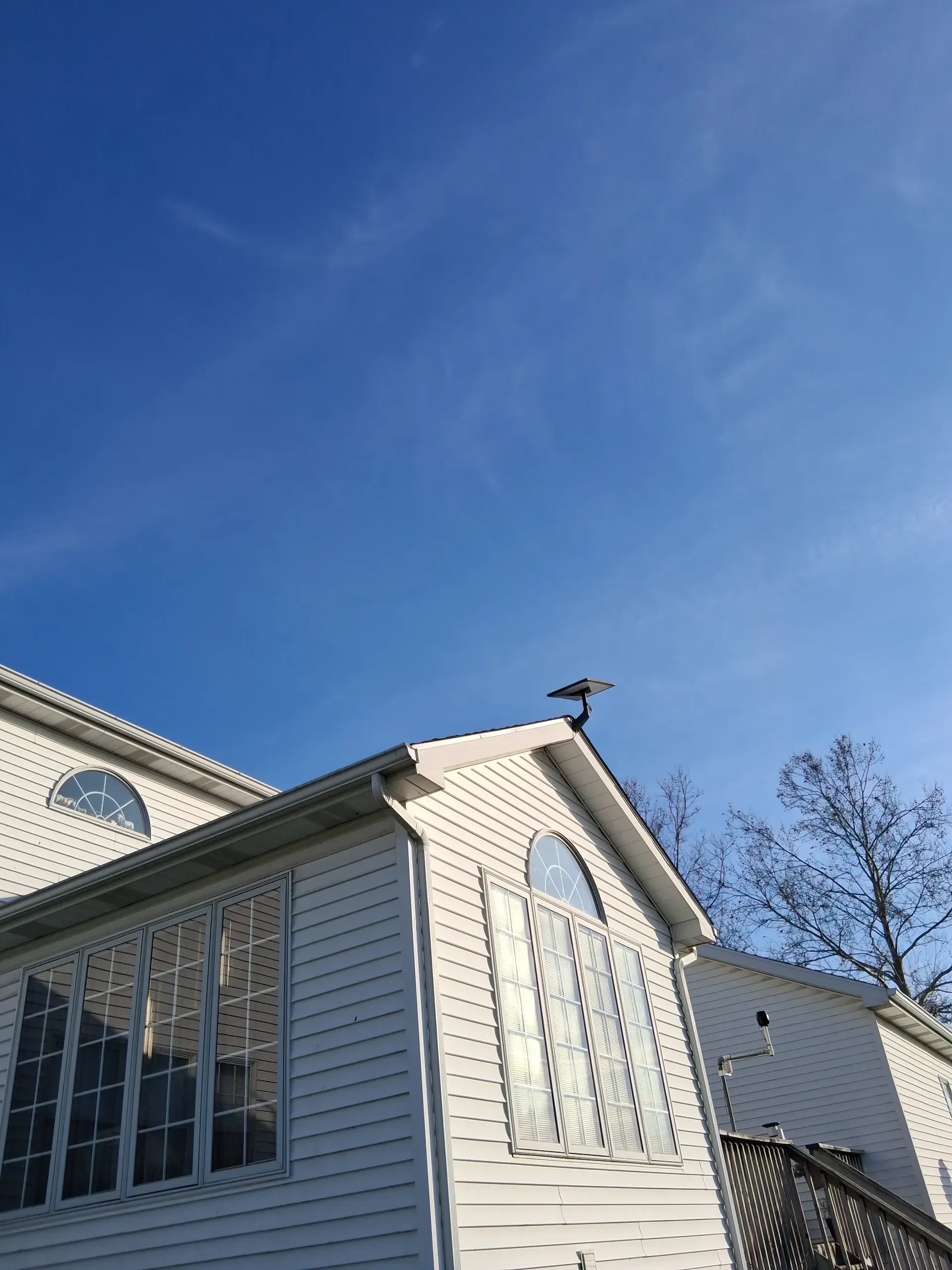 A bird perches on the roof peak of a white, multi-windowed building against a clear blue sky.