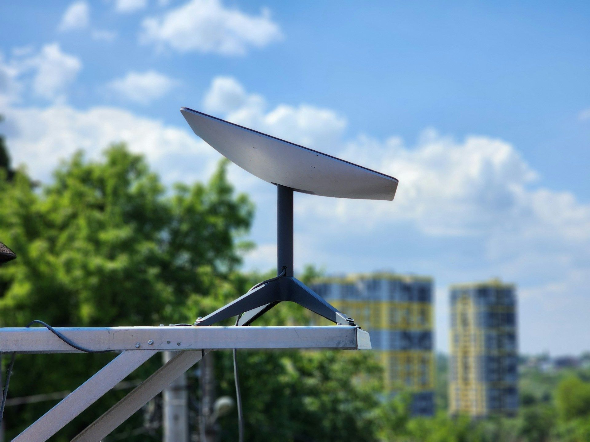 Starlink satellite dish on a tripod, mounted outdoors against a backdrop of trees and buildings.