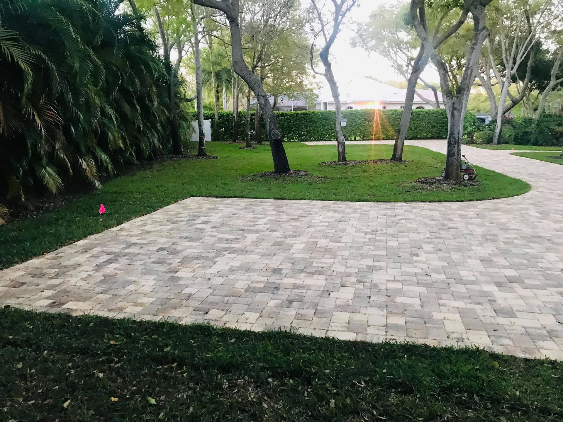 Stone patio in a landscaped garden with trees, grass, and a curved path at sunset.