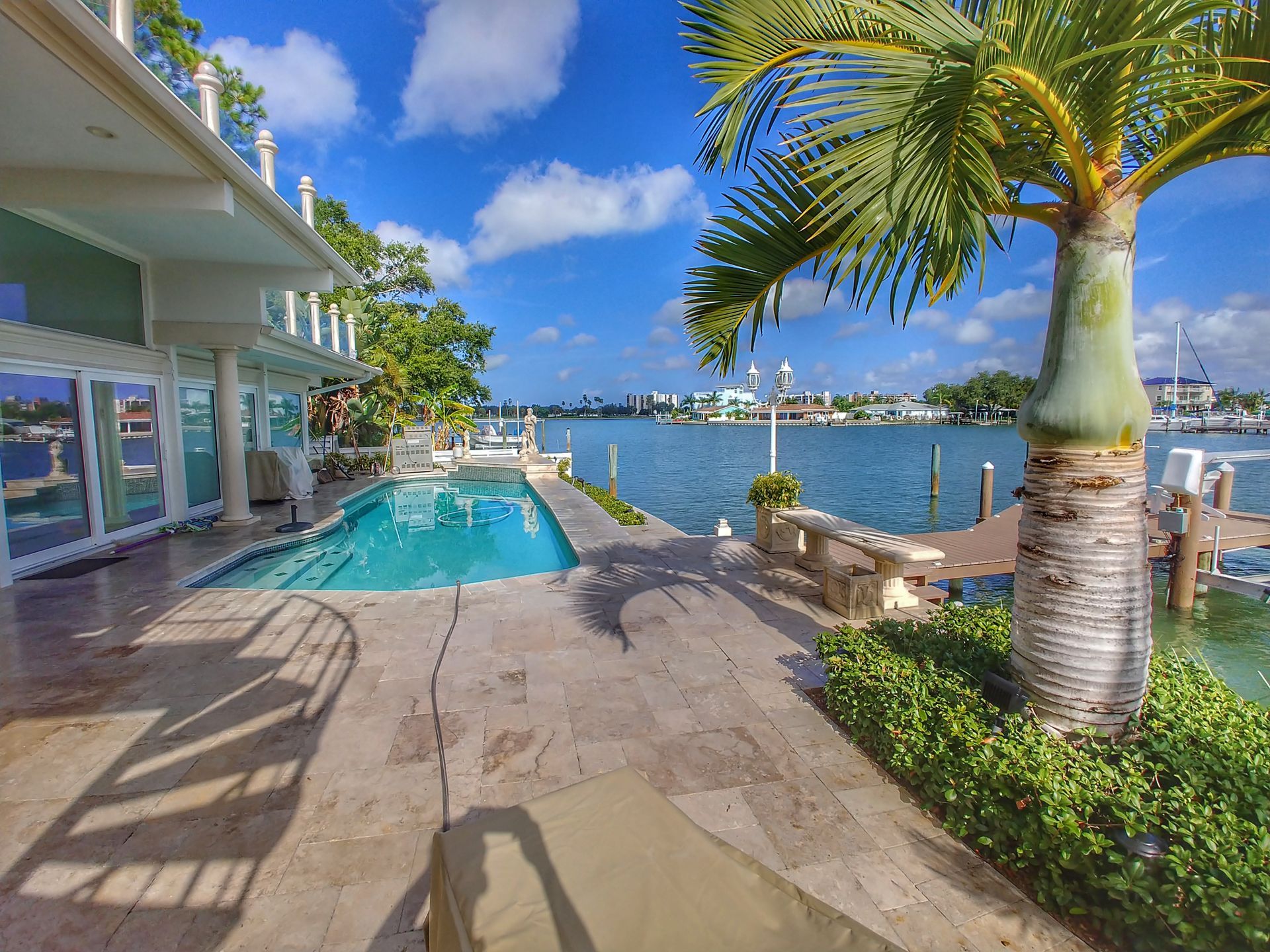 Tropical waterfront patio with a swimming pool, palm trees, and scenic water views under a blue Florida sky.