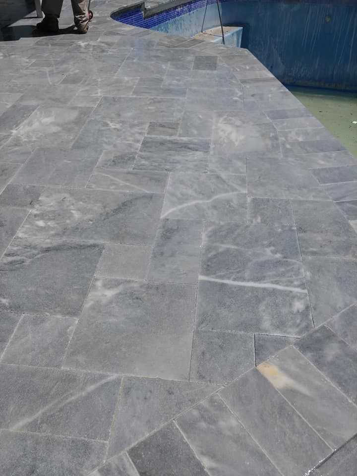 Gray marble walkway beside water, with a few people in the distance.