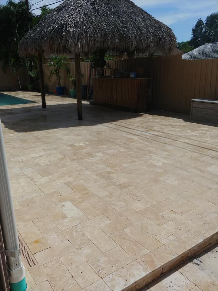 Patio with beige stone flooring, a thatched-roof palapa, and wooden fencing in bright sunlight