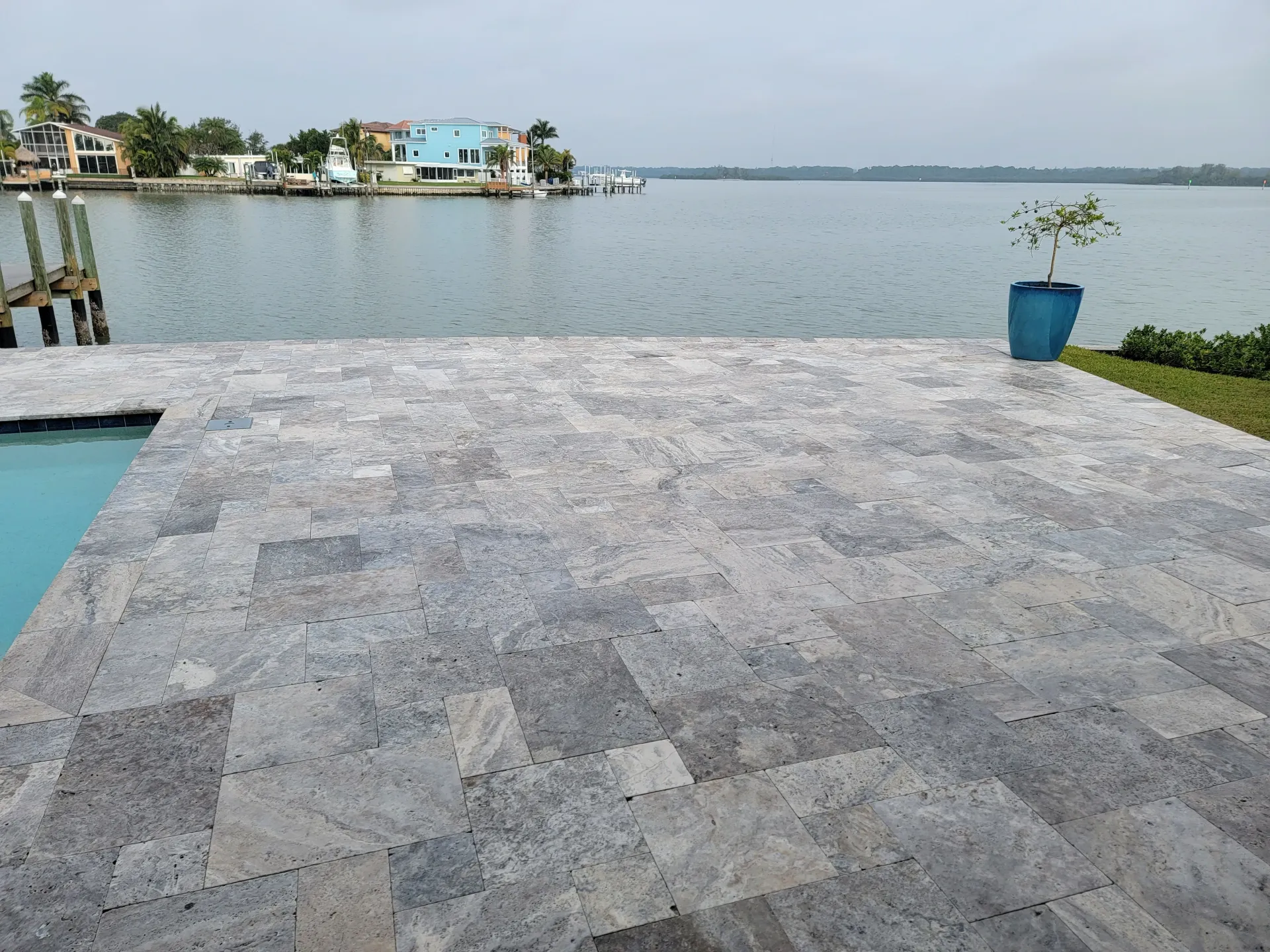 Gray travertine stone patio beside blue pool water, showing a textured tiled surface.