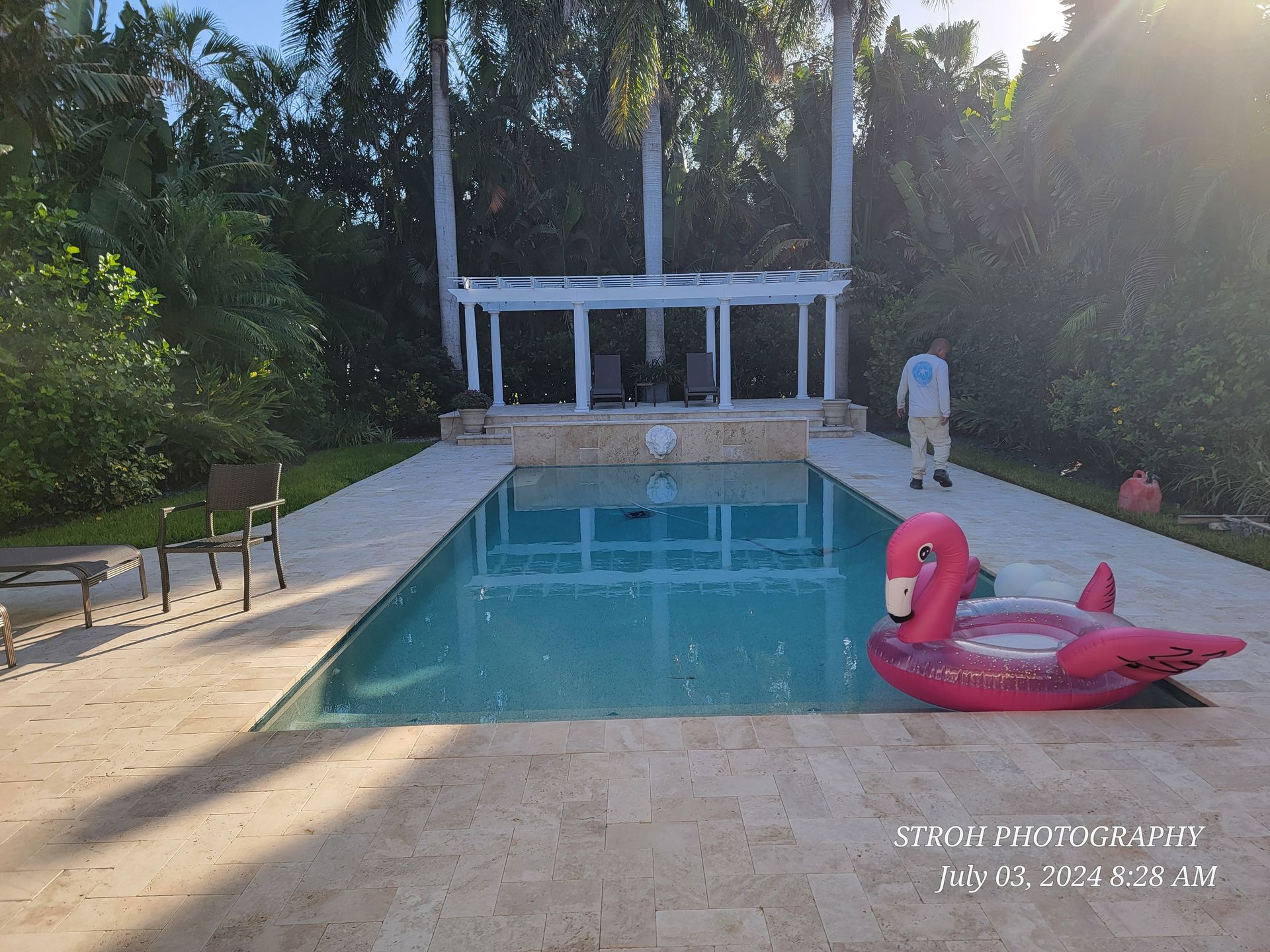 Backyard pool with a pink flamingo float and a person standing by the far end