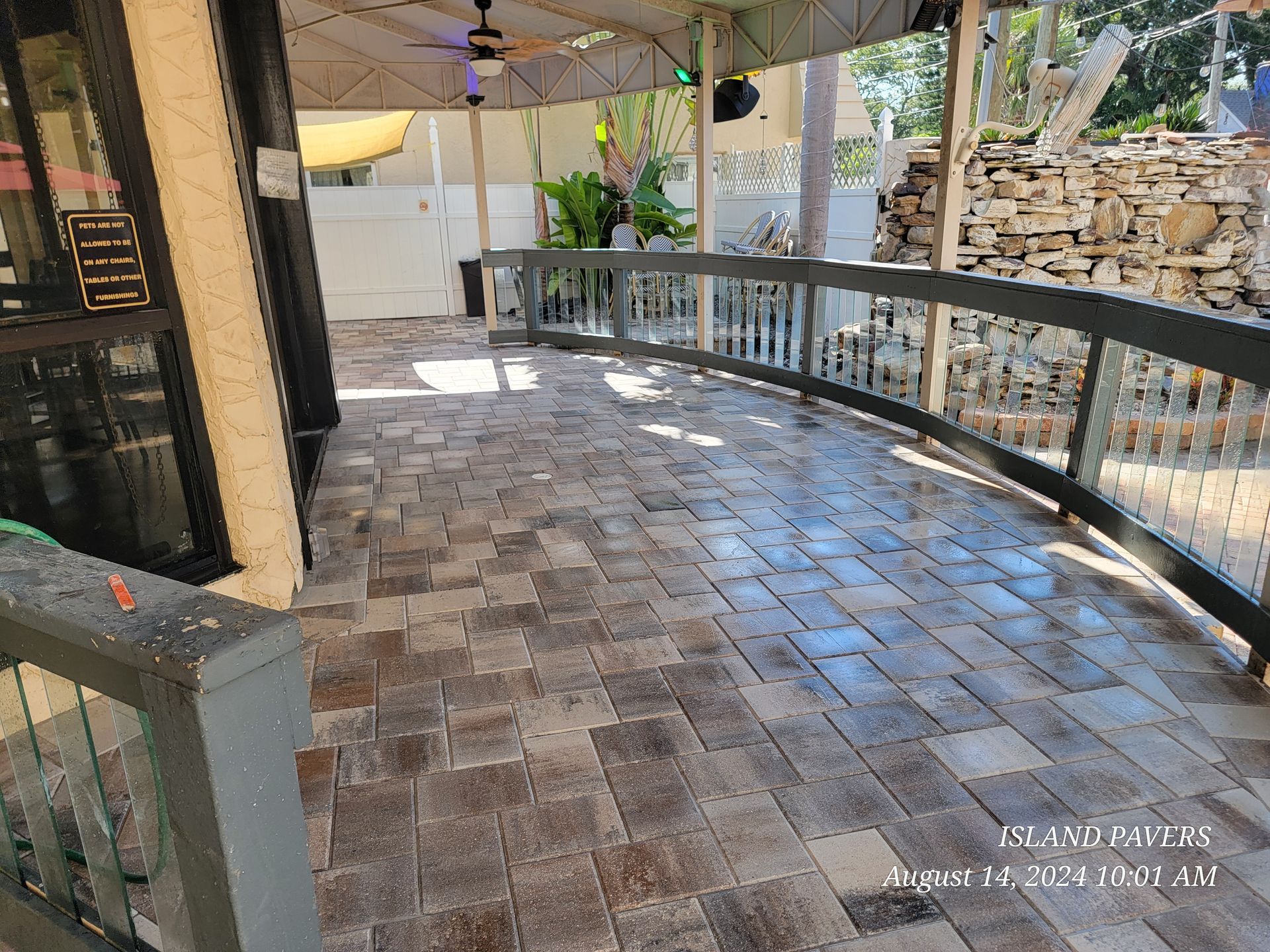 Stone tile patio with curved railing, ceiling fan, and scenic backyard views in a Florida outdoor space.