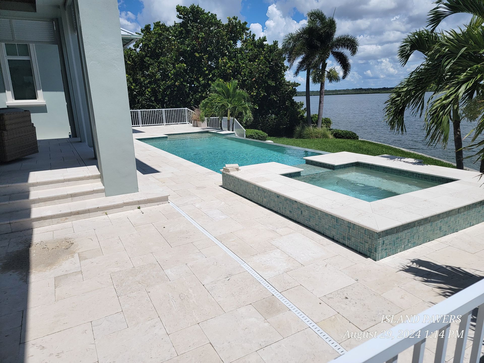Modern marble patio with white tile, a small hot tub, and an infinity pool overlooking the water