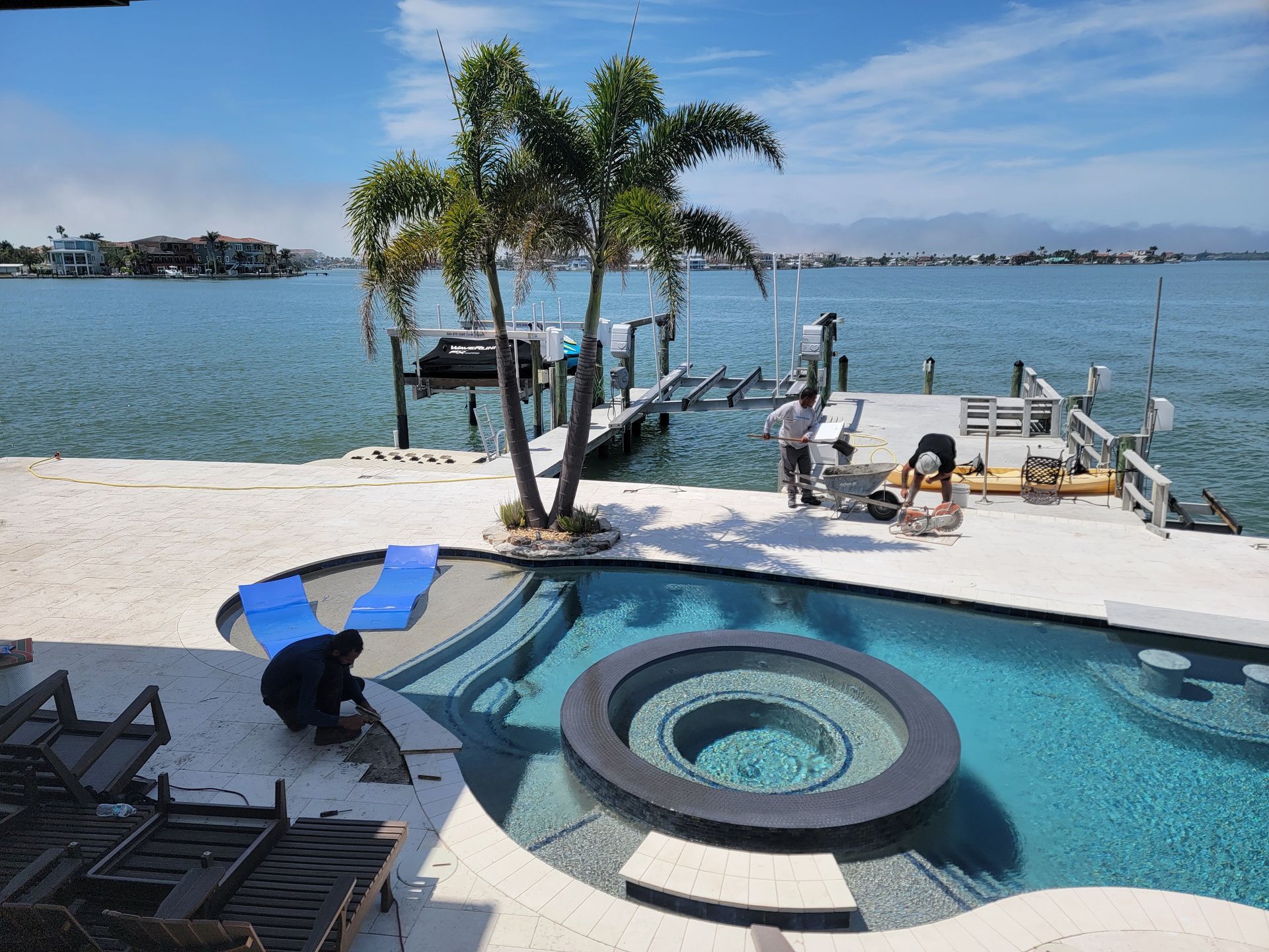 Tropical pool and spa overlooking the waterfront, featuring palm trees, lounge chairs, and sunny Florida views.