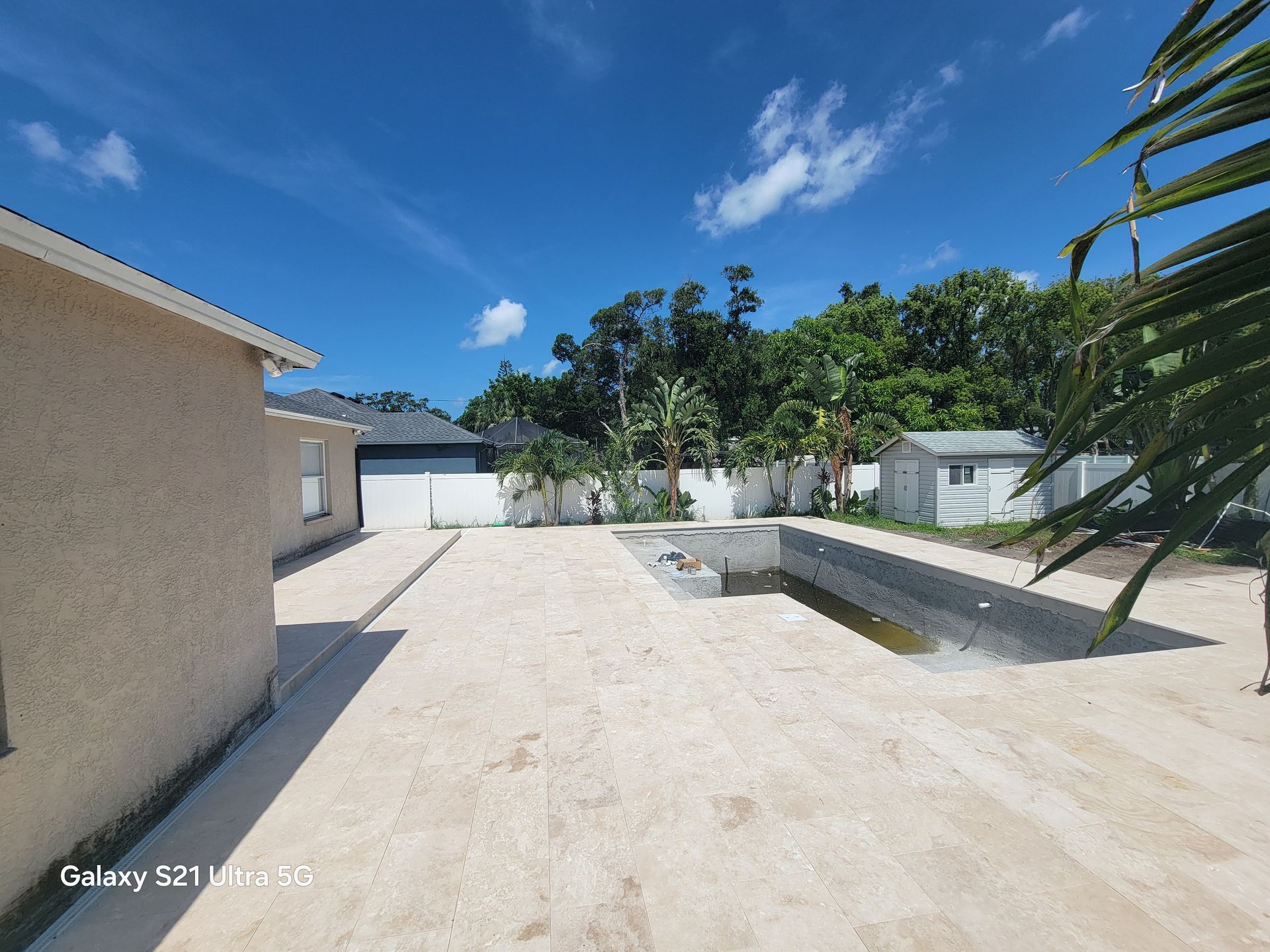 Sunny courtyard with white walls, sandy ground, blue sky, and a small pool or planter on the right.
