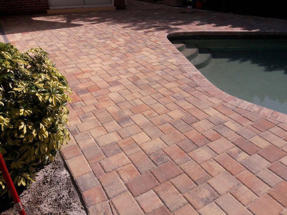 Brick patio beside a swimming pool, with a curved pool edge and shrubbery nearby
