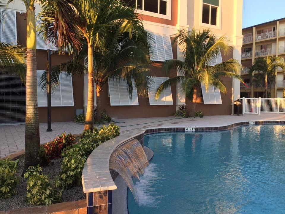 Palm-lined apartment pool with a curved water feature at sunset