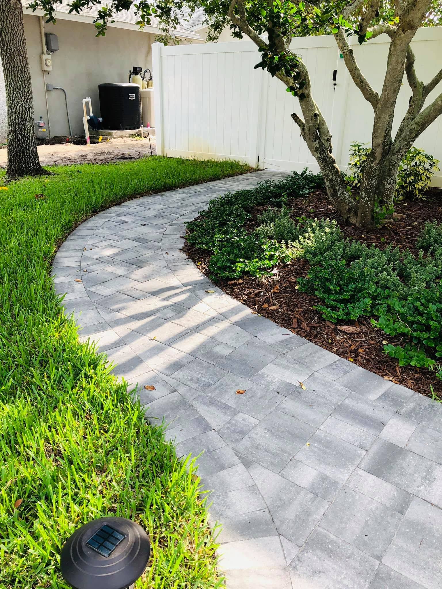 Curved stone walkway beside green lawn and trees in a sunny backyard