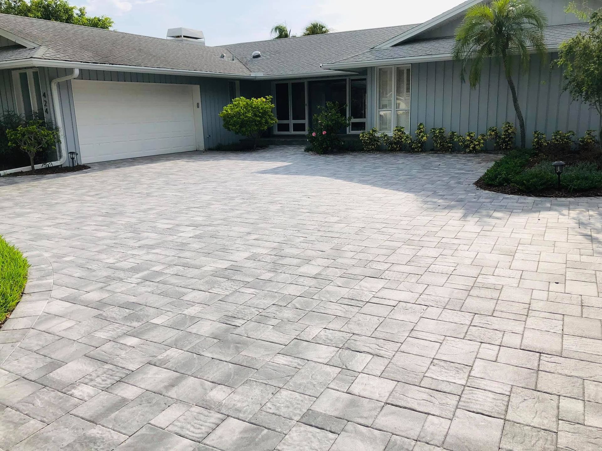 Suburban house with a light gray paver driveway, garage, and palm trees