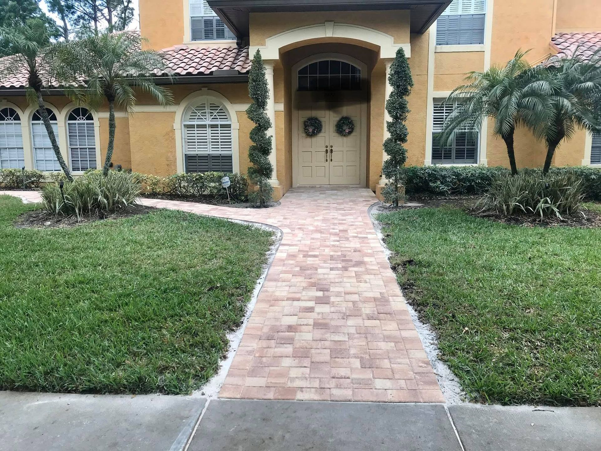 Brick walkway leading to a cream-colored house with arched entry and green lawn