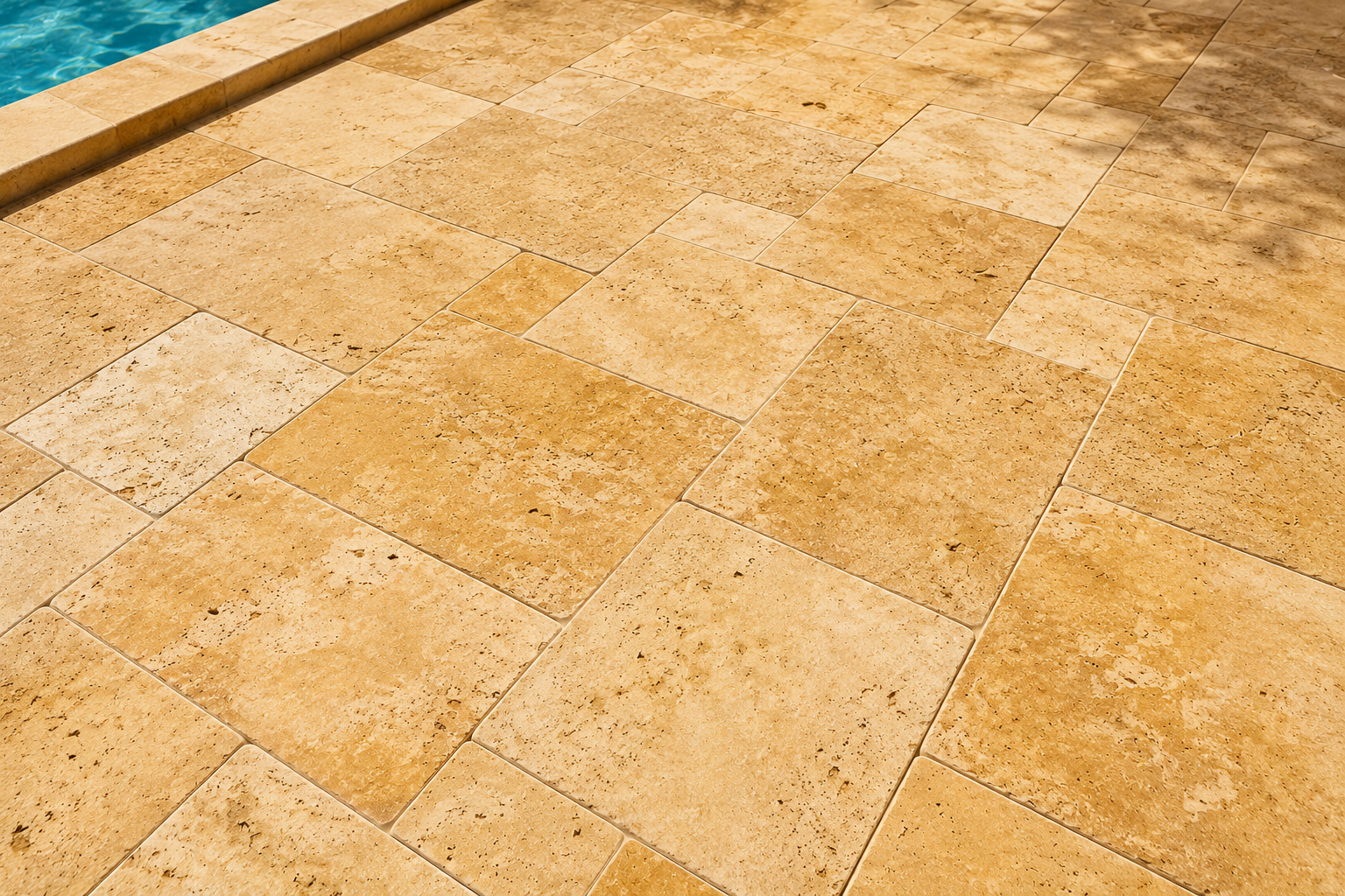 Close-up of tan marble paving tiles with a blue pool edge in the top left corner in florida