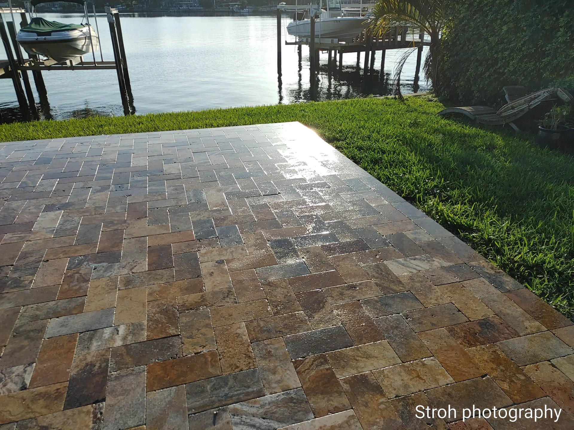 Poolside Florida patio with stone paving, steps, and a white house in bright sunlight.