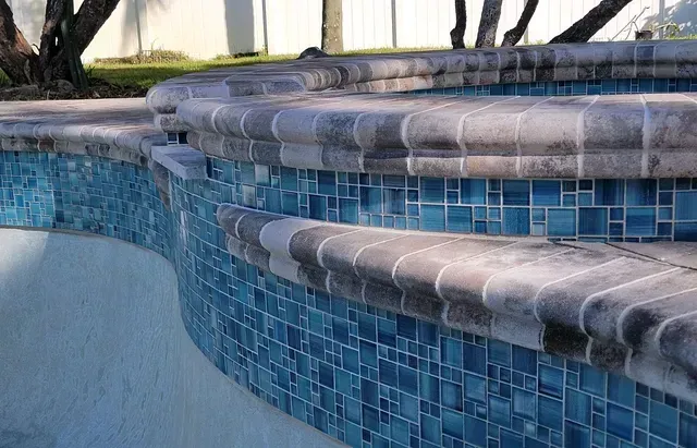 Blue tiled pool edge with curved stone coping and waterline tiles, showing a shallow pool wall.