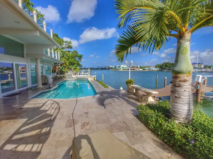 Poolside tropical garden with palm trees, green lawn, and a stone patio by the water