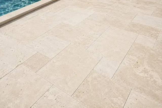 Close-up of tan marble paving tiles with a blue pool edge in the top left corner in florida