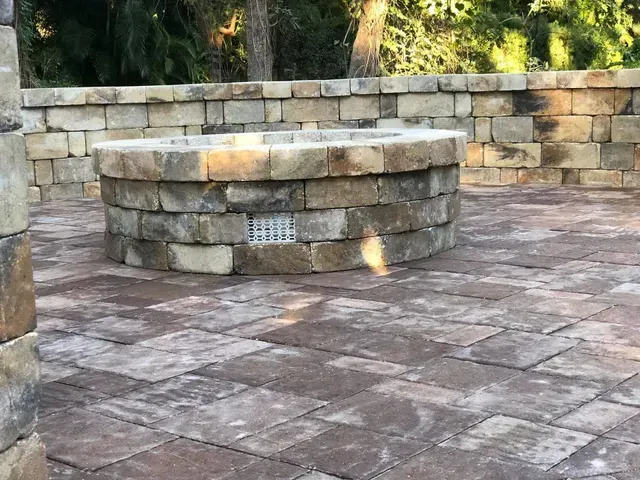 Stone fire pit in a paved patio with stacked stone wall backdrop