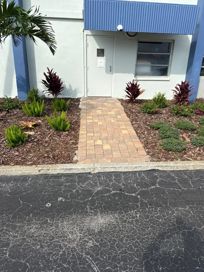 Stepping-stone path of rectangular pavers through dark gravel beside hedges and a wall, leading to a gate