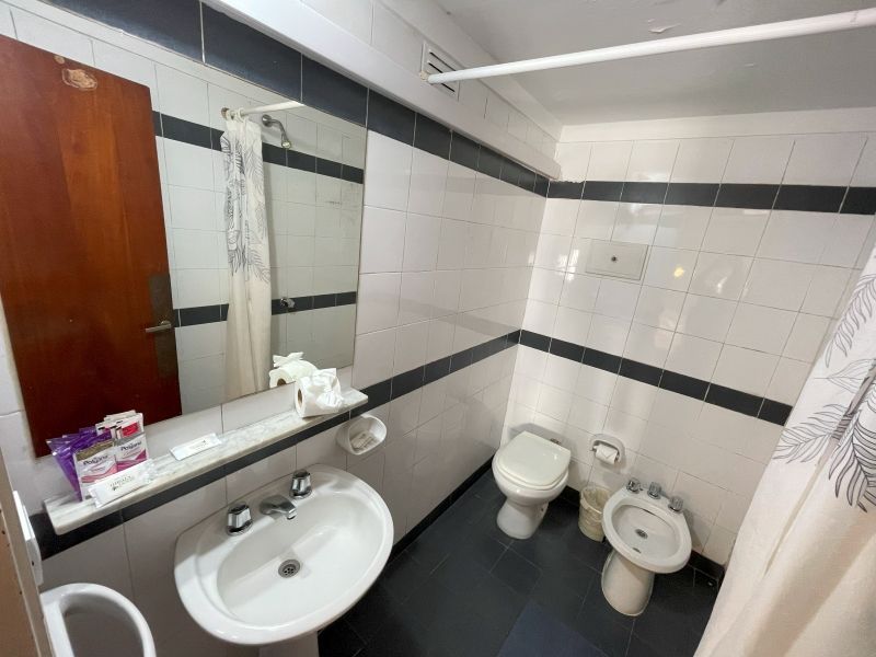 Bathroom with white tiled walls, dark floor, toilet, bidet, sink, mirror, and shower curtain.