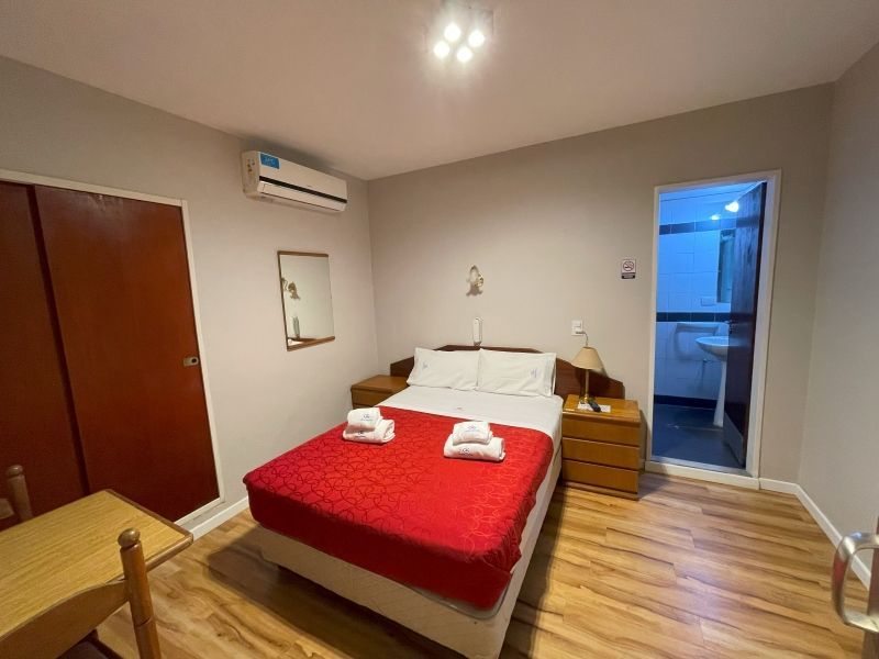 Dormitorio con colcha roja, muebles de madera y puerta de baño abierta.