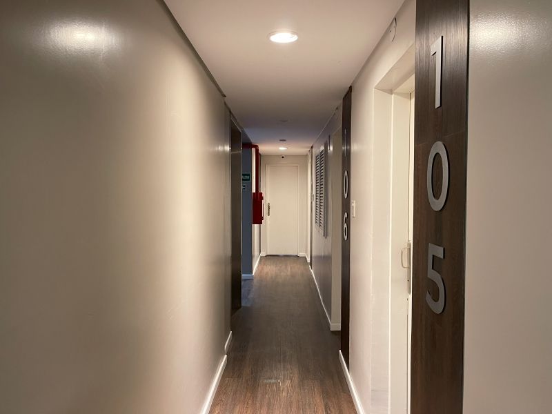 Narrow hallway with doors and room number 105. Dark wood floor, white walls, and a red fire extinguisher.