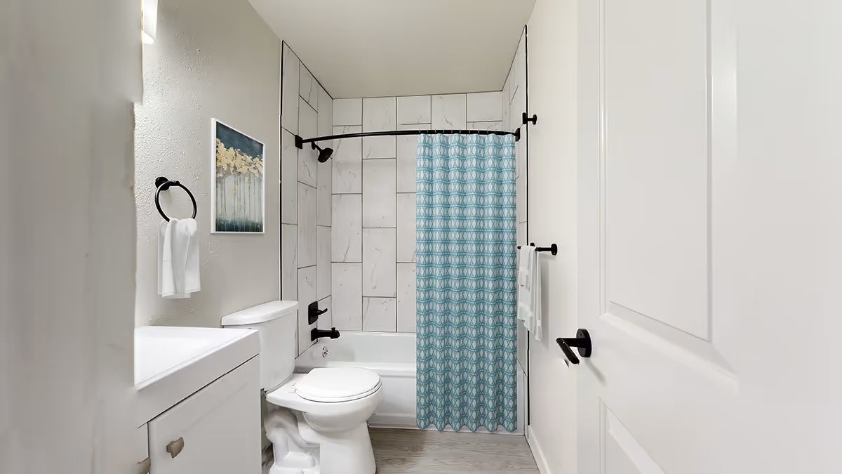 A small, bright bathroom with a white vanity, toilet, and a bathtub enclosed by a blue-and-white patterned shower curtain.