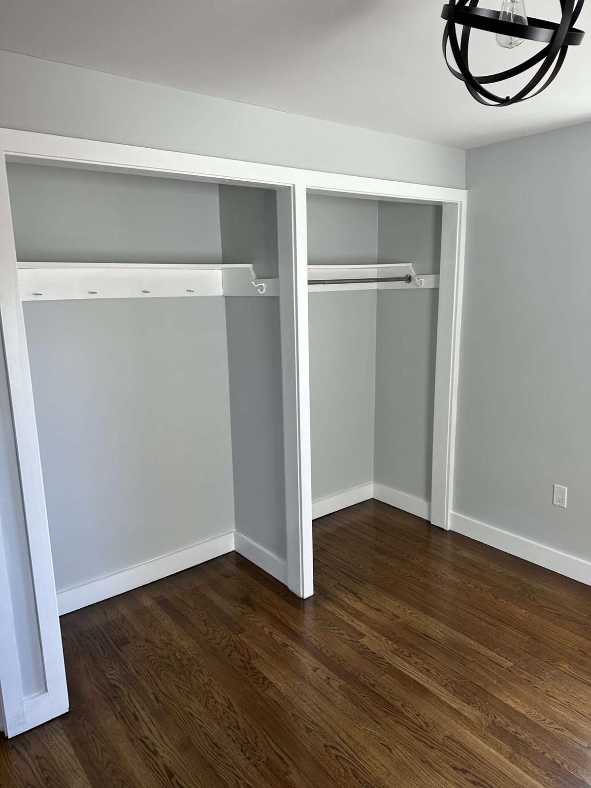 A bedroom with hardwood floors and a closet with a chandelier hanging from the ceiling.