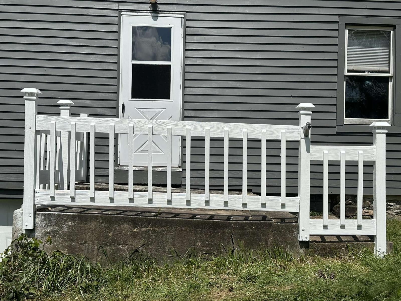 A white fence is in front of a gray house.