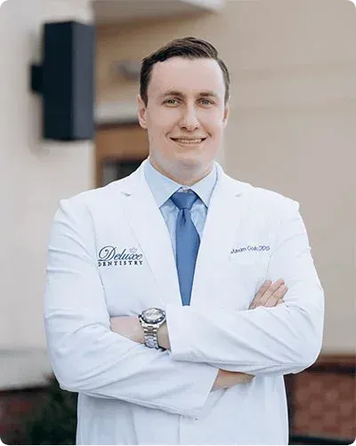 Dr. Maxim Godko smiling with arms crossed in his white coat, the dentist who leads your gum care while his hygiene team performs your deep cleaning