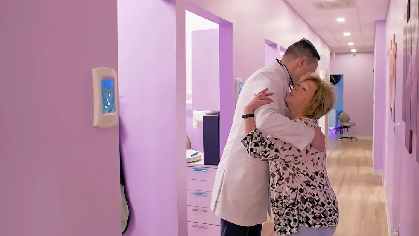 Dr. Maxim Godko hugging a happy patient in the office hallway after her dental checkup