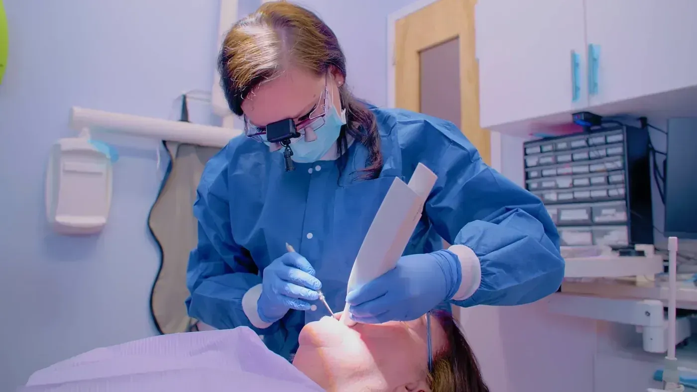 Deluxe hygienist wearing magnifying loupes cleaning a patient’s teeth during a routine dental cleaning