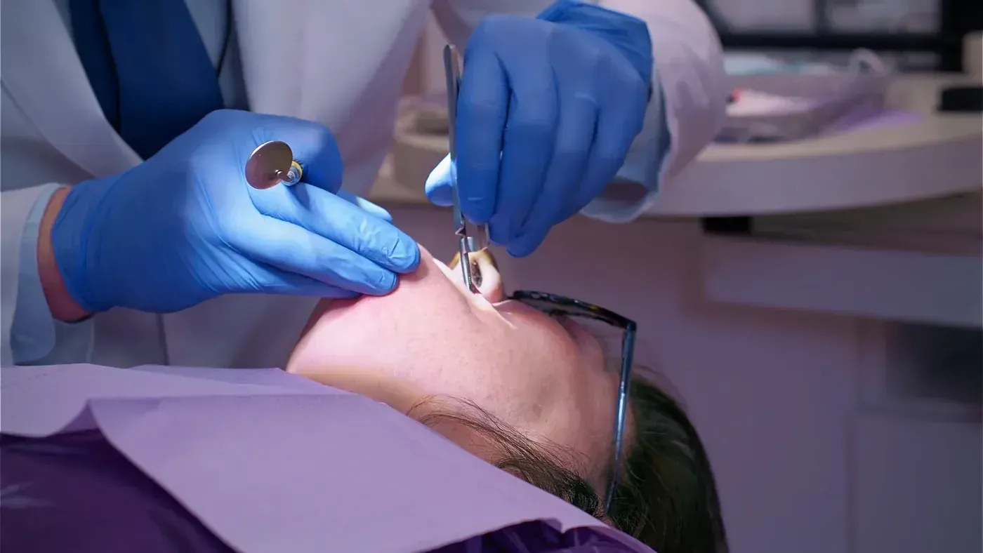 Hygienist checking a patient’s teeth with a mirror so his gums are healthy before braces or Invisalign begin