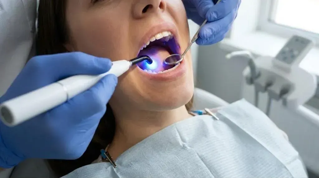 Gloved hands holding a curing light to harden tooth-colored resin during dental bonding