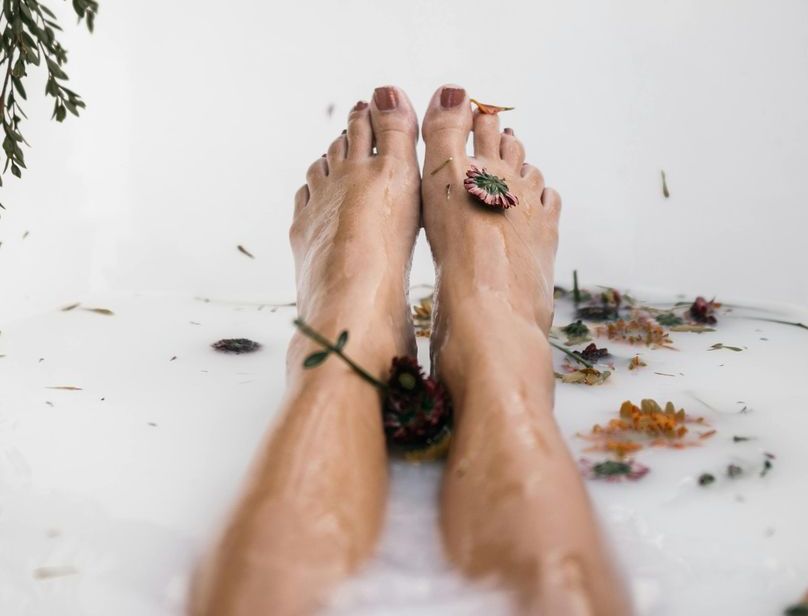A pair of legs submerged in a milky bathwater, decorated with scattered flower petals.