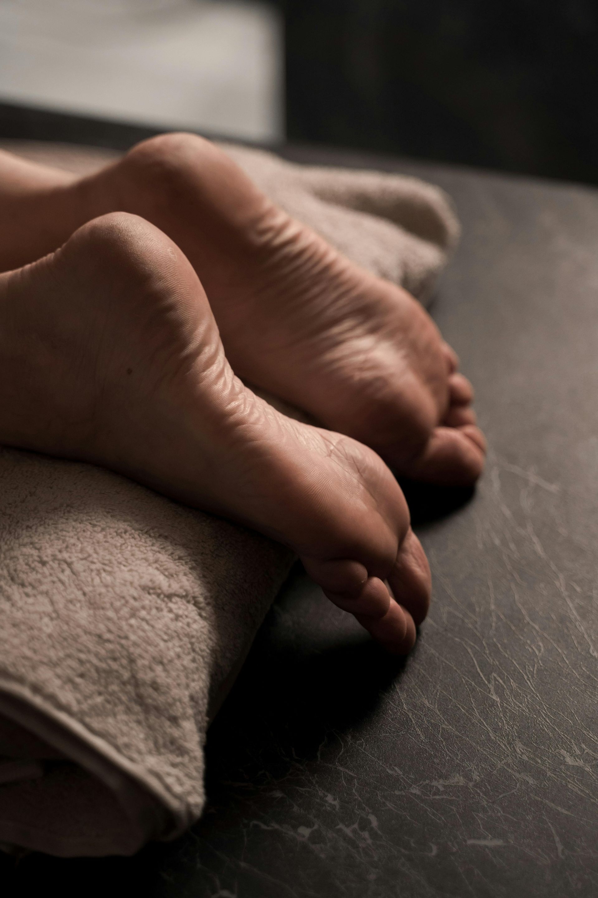Close-up of bare feet resting on a tan folded towel against a dark, textured surface.