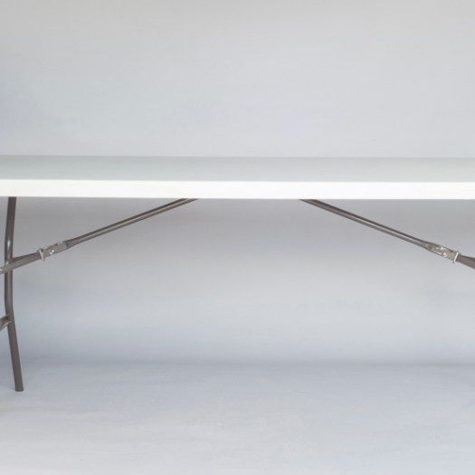 White folding table with metal cross braces against a plain light wall and floor