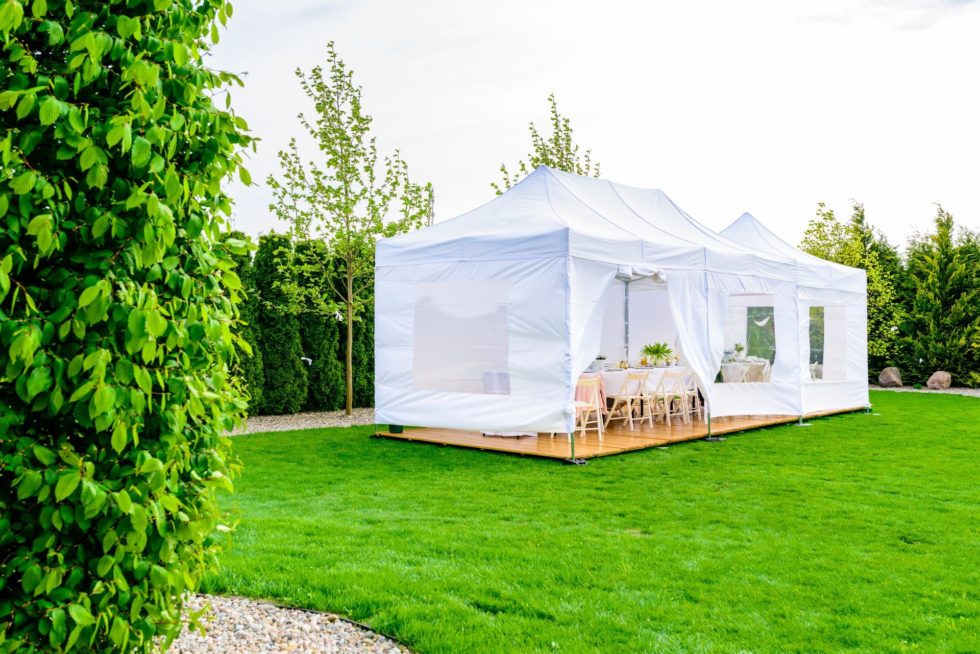 White outdoor wedding ceremony setup with aisle, chairs, and floral canopy in a garden-like setting