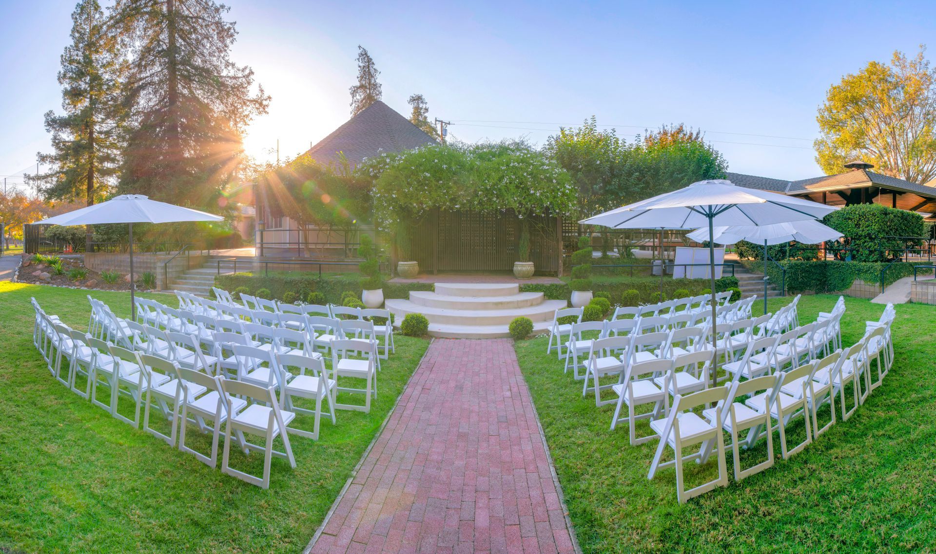 Outdoor wedding setup with white chairs, central aisle, and tents on a sunny lawn