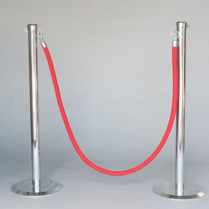 Red velvet rope between two silver stanchions on a gray background